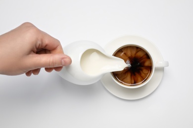 Photo of Woman pouring milk into cup of coffee on white background, top view