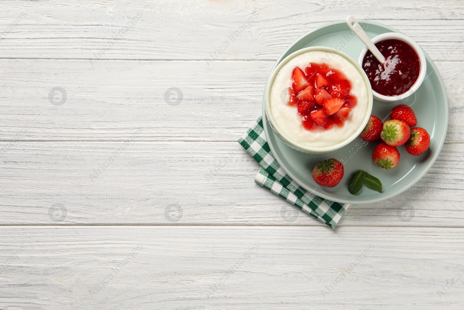 Photo of Delicious semolina pudding with strawberries and jam on white wooden table, top view. Space for text