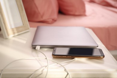 Smartphone with wireless charger connected to laptop on white table in bedroom