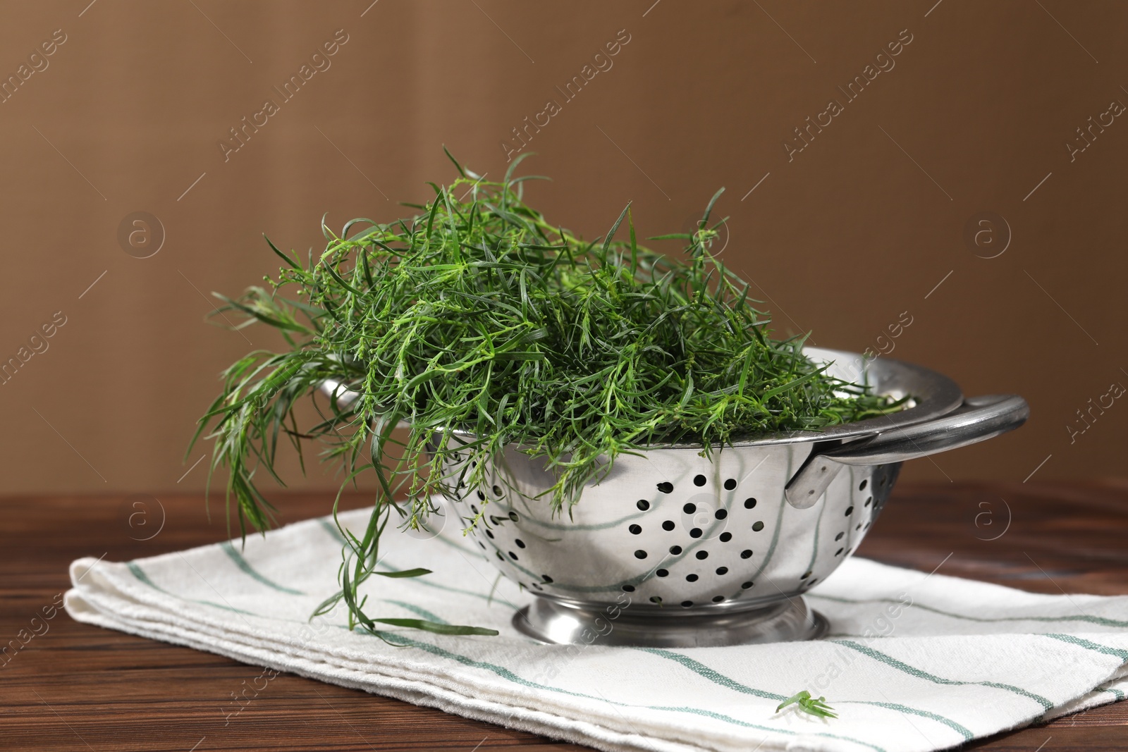 Photo of Colander with fresh tarragon leaves on wooden table