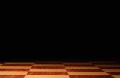 Photo of Checkered chessboard on dark background, closeup. Space for text