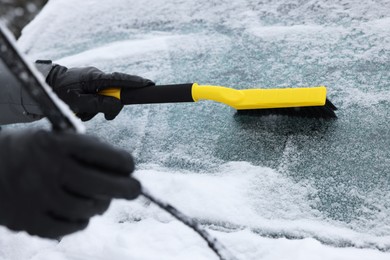 Photo of Man cleaning snow from car windshield outdoors, closeup