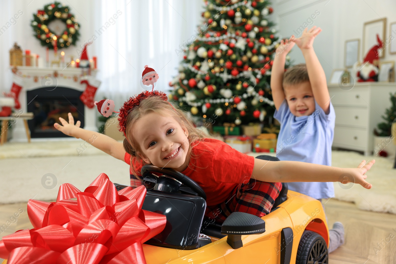 Photo of Cute little children playing with toy car in room decorated for Christmas