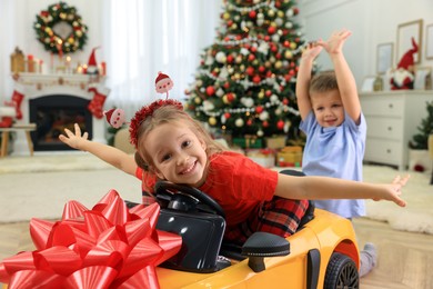 Cute little children playing with toy car in room decorated for Christmas