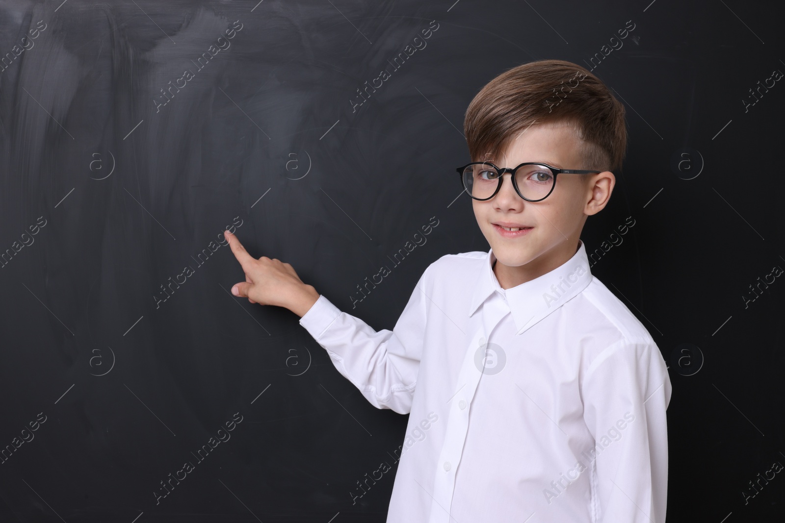 Photo of Cute schoolboy in glasses near chalkboard, space for text