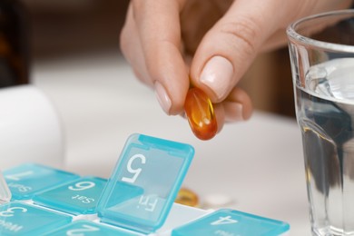 Woman taking pill from plastic box indoors, closeup