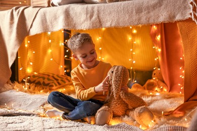 Photo of Boy playing with toy bunny in play tent at home
