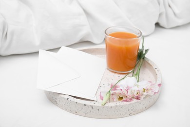 Photo of Tray with glass of juice, flowers and envelope on white bed