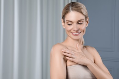 Photo of Happy woman applying body oil onto shoulder indoors, space for text