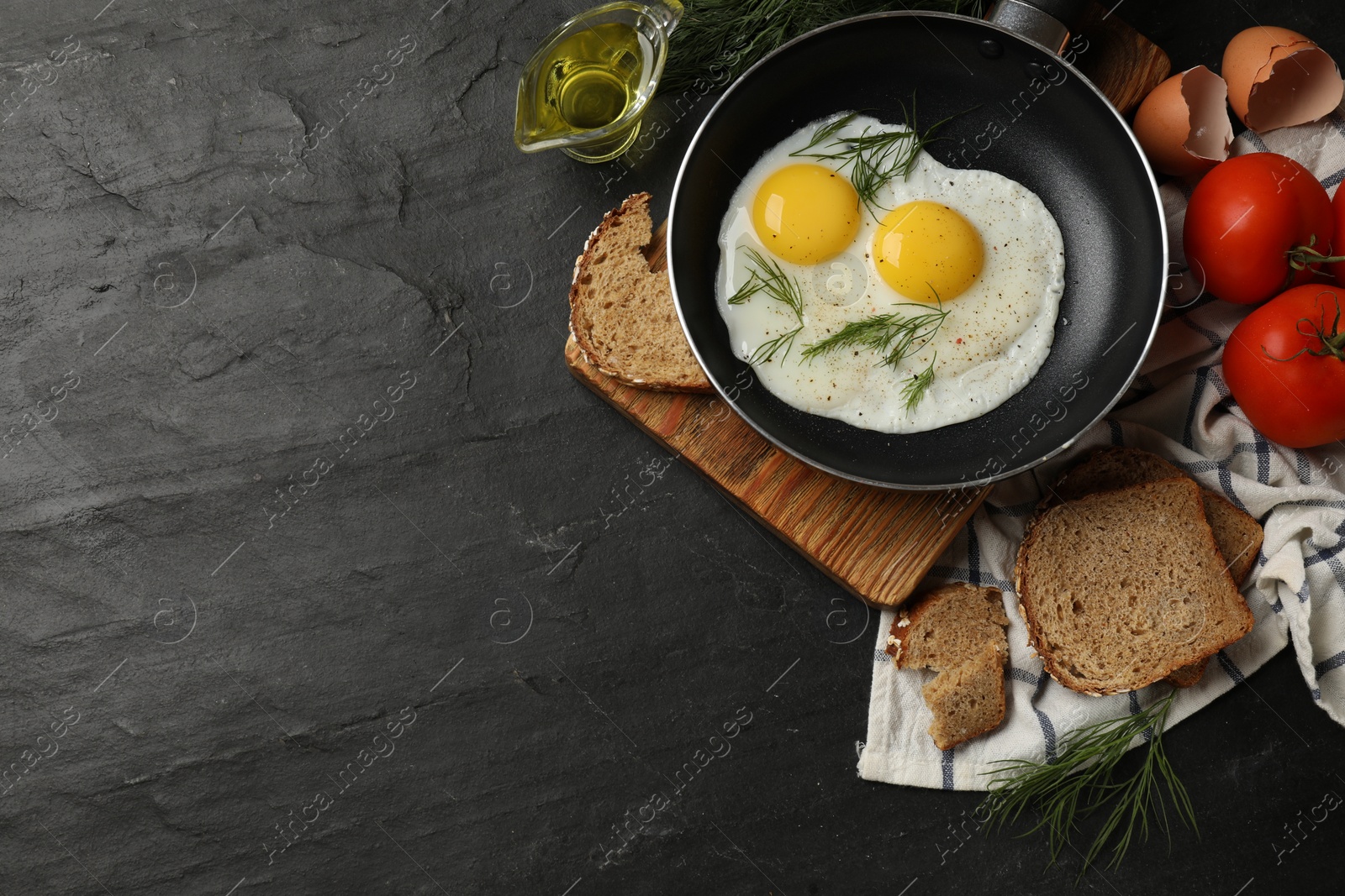 Photo of Frying pan with tasty cooked eggs and other products on black table, flat lay. Space for text