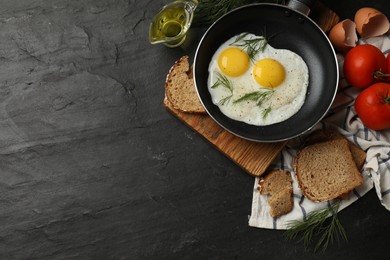 Frying pan with tasty cooked eggs and other products on black table, flat lay. Space for text