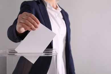 Photo of Woman putting her vote into ballot box on light grey background, closeup. Space for text