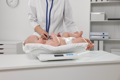 Photo of Pediatrician weighting and examining cute little baby with stethoscope in clinic, closeup