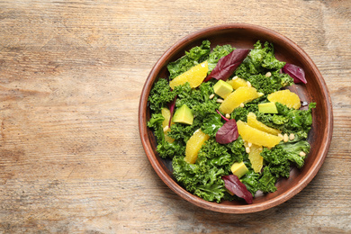 Photo of Tasty fresh kale salad on wooden table, top view. Space for text