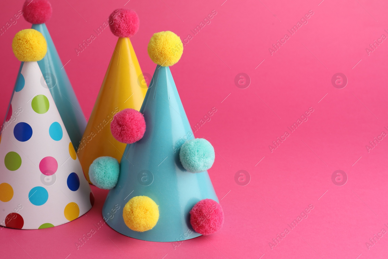 Photo of Beautiful party hats with pompoms on pink background, space for text