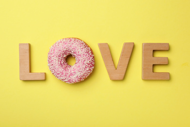 Word LOVE made with wooden letters and donut on yellow background, flat lay