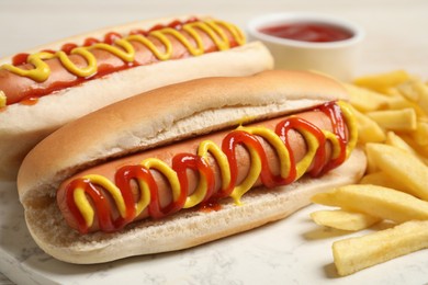 Delicious hot dogs with mustard, ketchup and potato fries on table, closeup
