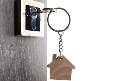 Photo of Mortgage and real estate. Open door with key and house shaped keychain on white background, space for text