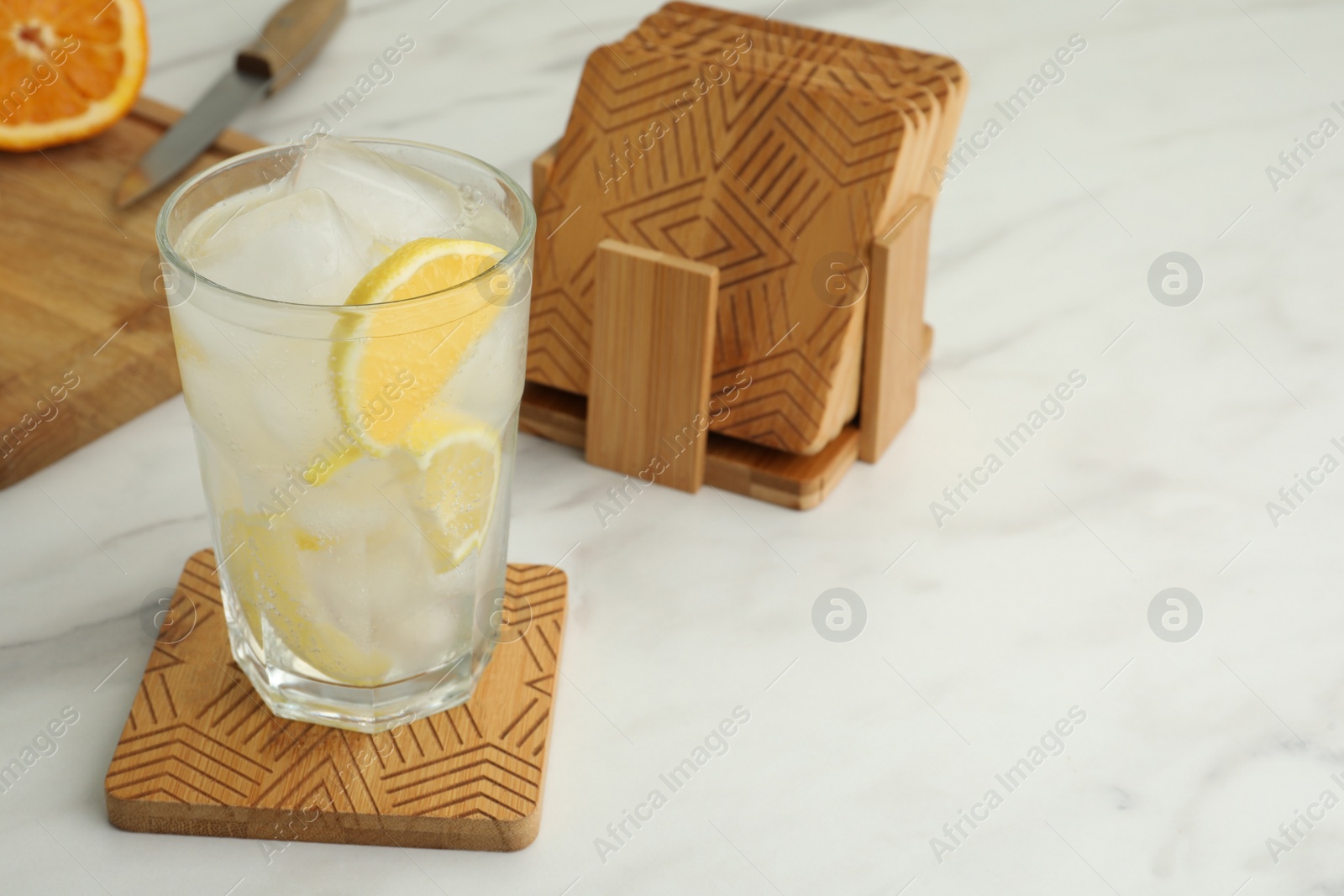 Photo of Glass of cocktail and stylish wooden cup coasters on white table