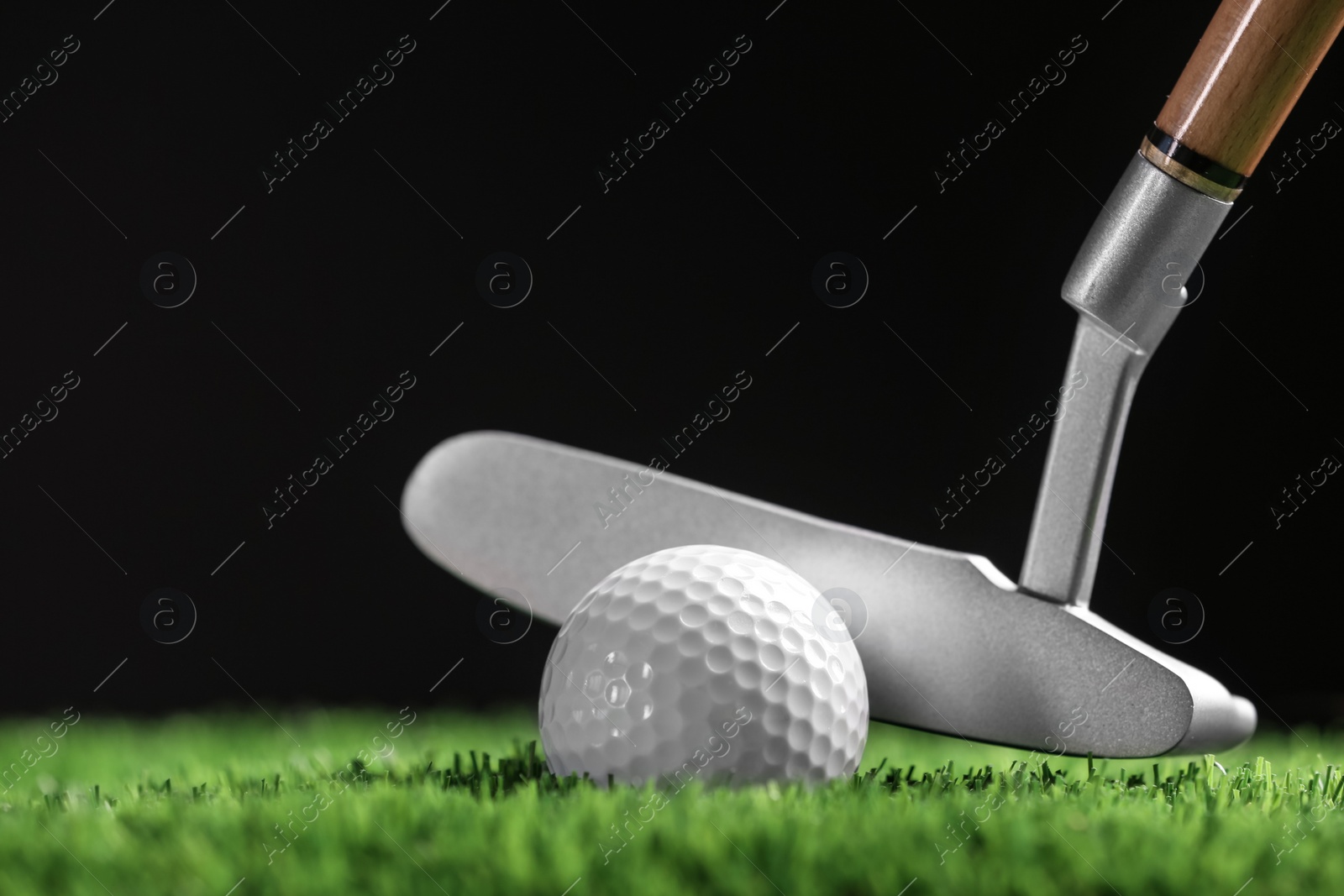 Photo of Hitting golf ball with club on artificial grass against black background, space for text