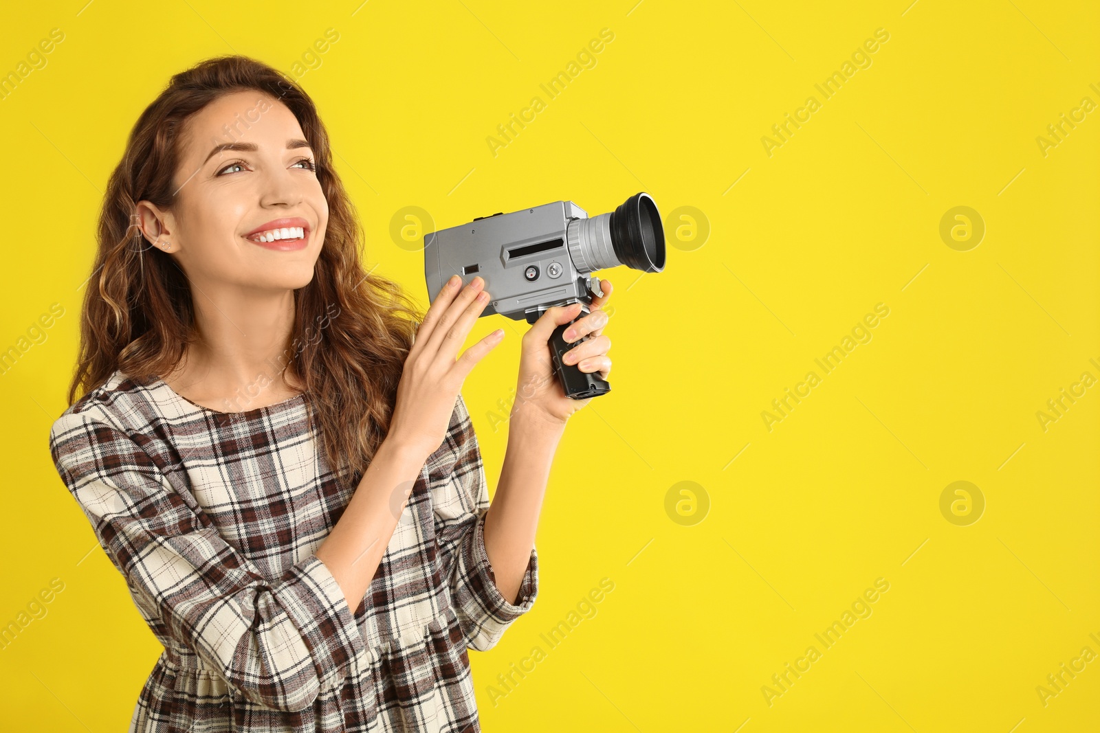 Photo of Beautiful young woman with vintage video camera on yellow background, space for text