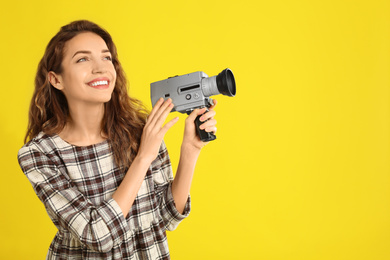 Beautiful young woman with vintage video camera on yellow background, space for text