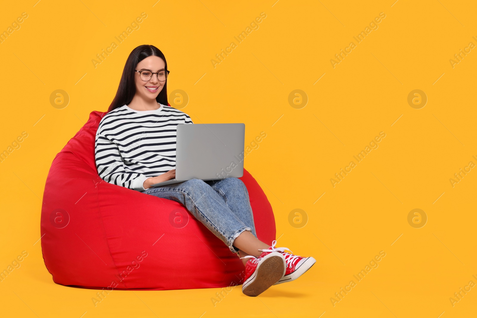 Photo of Happy woman with laptop sitting on beanbag chair against orange background