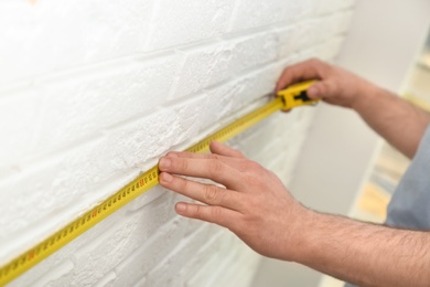 Photo of Man measuring brick wall indoors, closeup. Construction tool