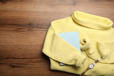 Photo of Yellow warm sweater with book and wristwatch on wooden table, flat lay. Space for text