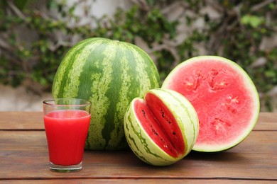 Delicious ripe watermelons and glass of fresh juice on wooden table outdoors