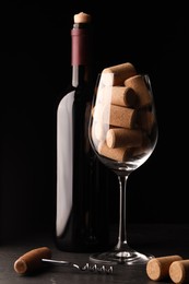 Bottle of wine, glass with corks and corkscrew on black table