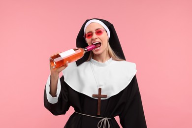 Photo of Woman in nun habit and sunglasses holding bottle of wine on pink background
