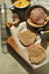 Cooking schnitzel. Raw pork chops in bread crumbs, meat mallet and ingredients on grey table, flat lay