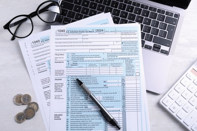 Tax forms, coins, pen, laptop and calculator on light grey table, flat lay