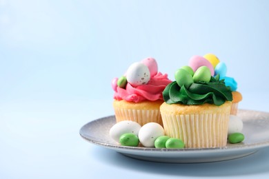 Photo of Tasty cupcakes with Easter decor on light blue background, space for text