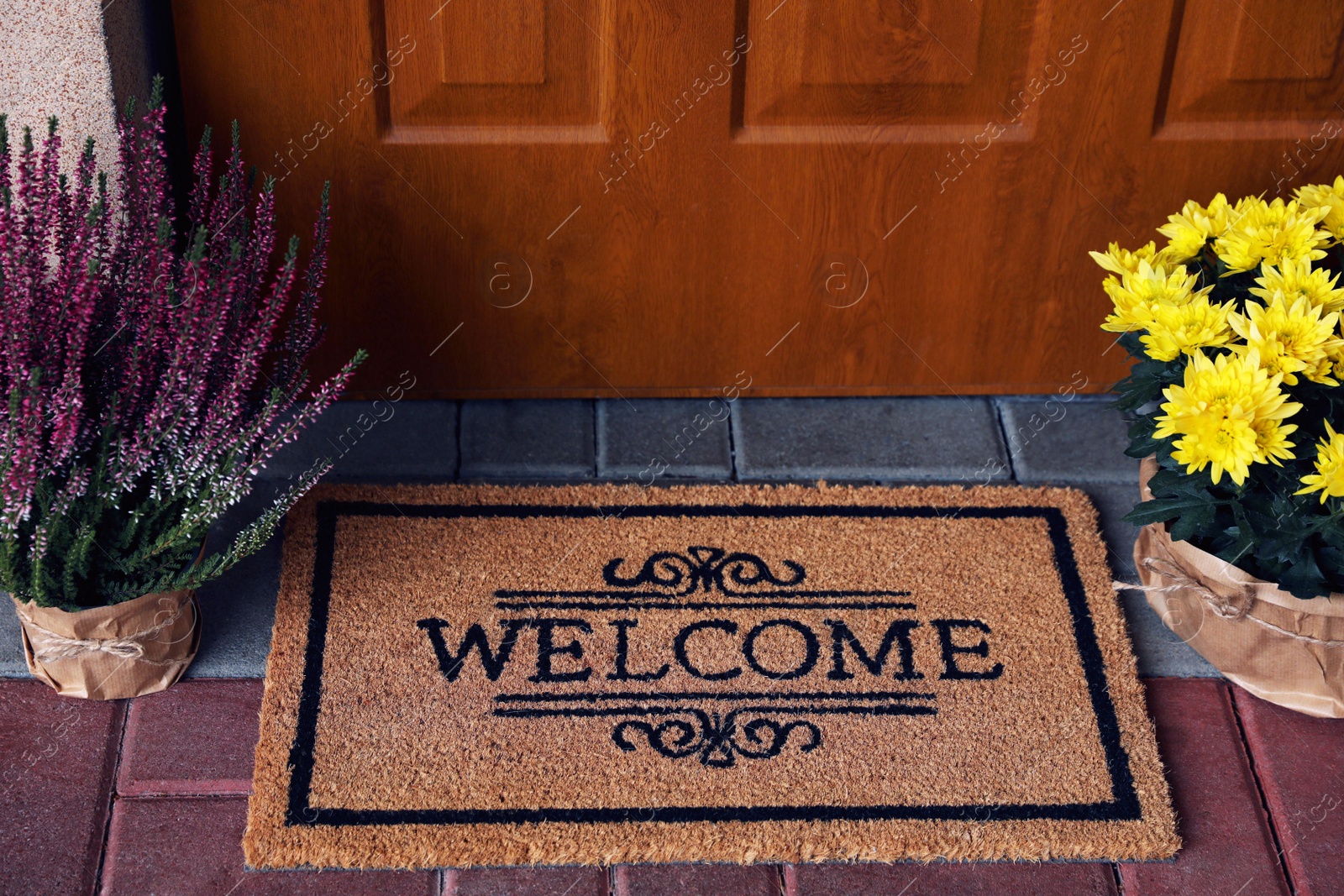 Photo of Door mat with word Welcome and beautiful flowers near entrance