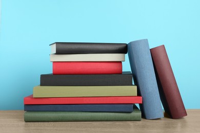Photo of Many hardcover books on wooden table near light blue wall