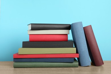 Many hardcover books on wooden table near light blue wall