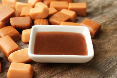 Delicious caramel candies and sauce on wooden background