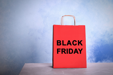 Paper shopping bag with phrase BLACK FRIDAY on table against color background