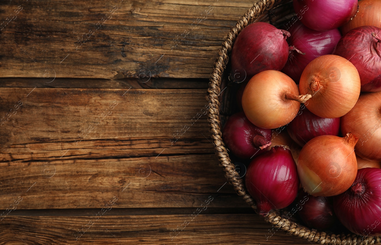 Photo of Onion bulbs in basket on wooden table, top view. Space for text