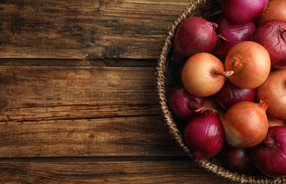 Onion bulbs in basket on wooden table, top view. Space for text