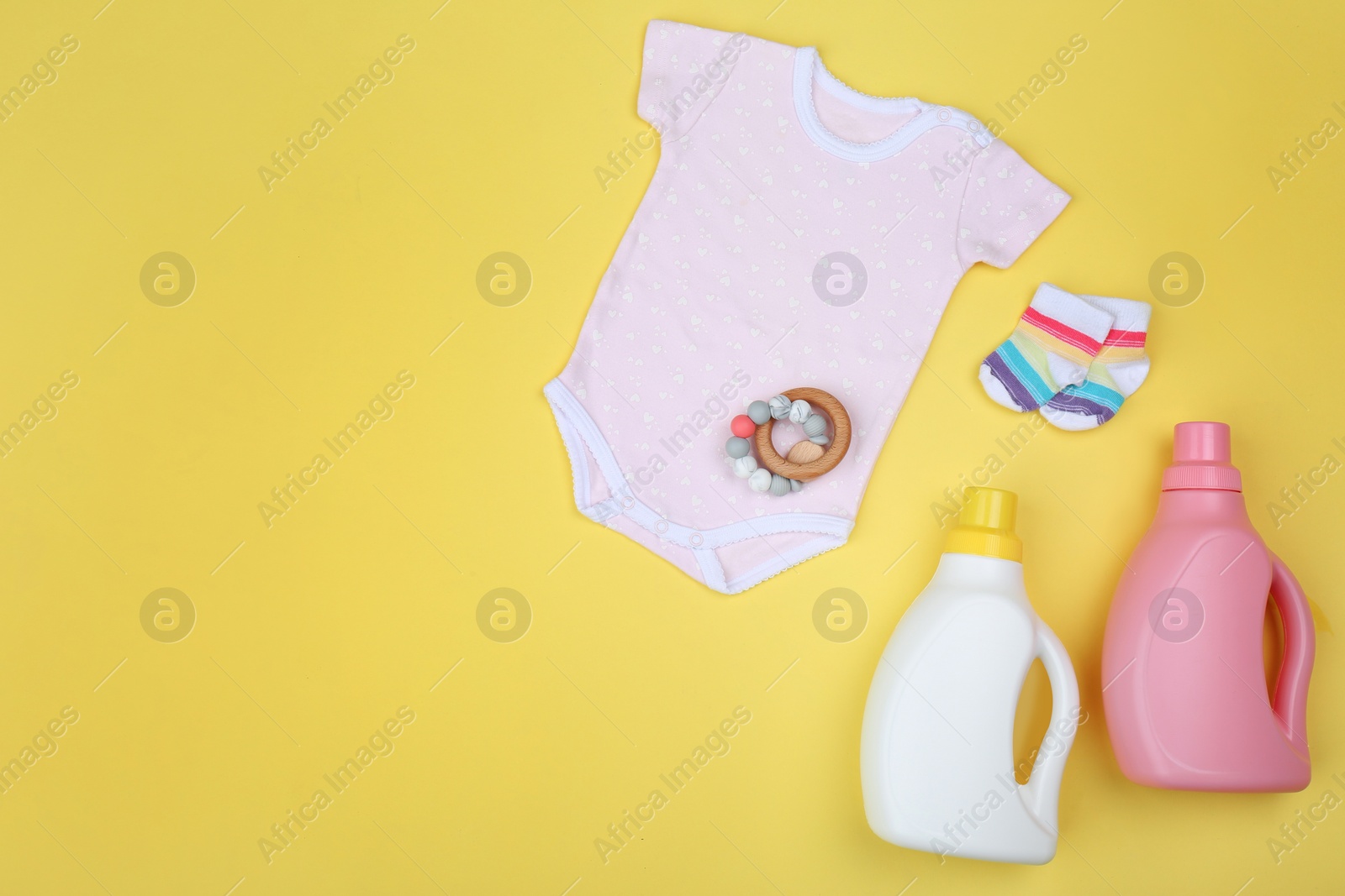 Photo of Flat lay composition with detergents and children's clothes on yellow background. Space for text