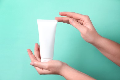 Photo of Woman with tube of hand cream on turquoise background, closeup