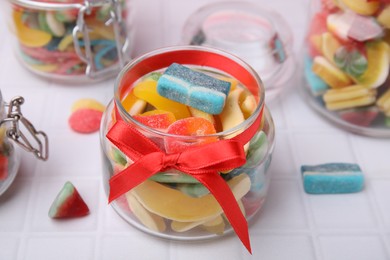 Glass jars with tasty colorful jelly candies on white tiled table, closeup