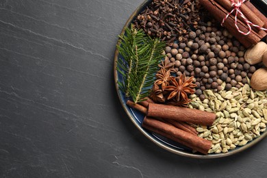 Different spices, nuts and fir branches on dark gray textured table, top view. Space for text