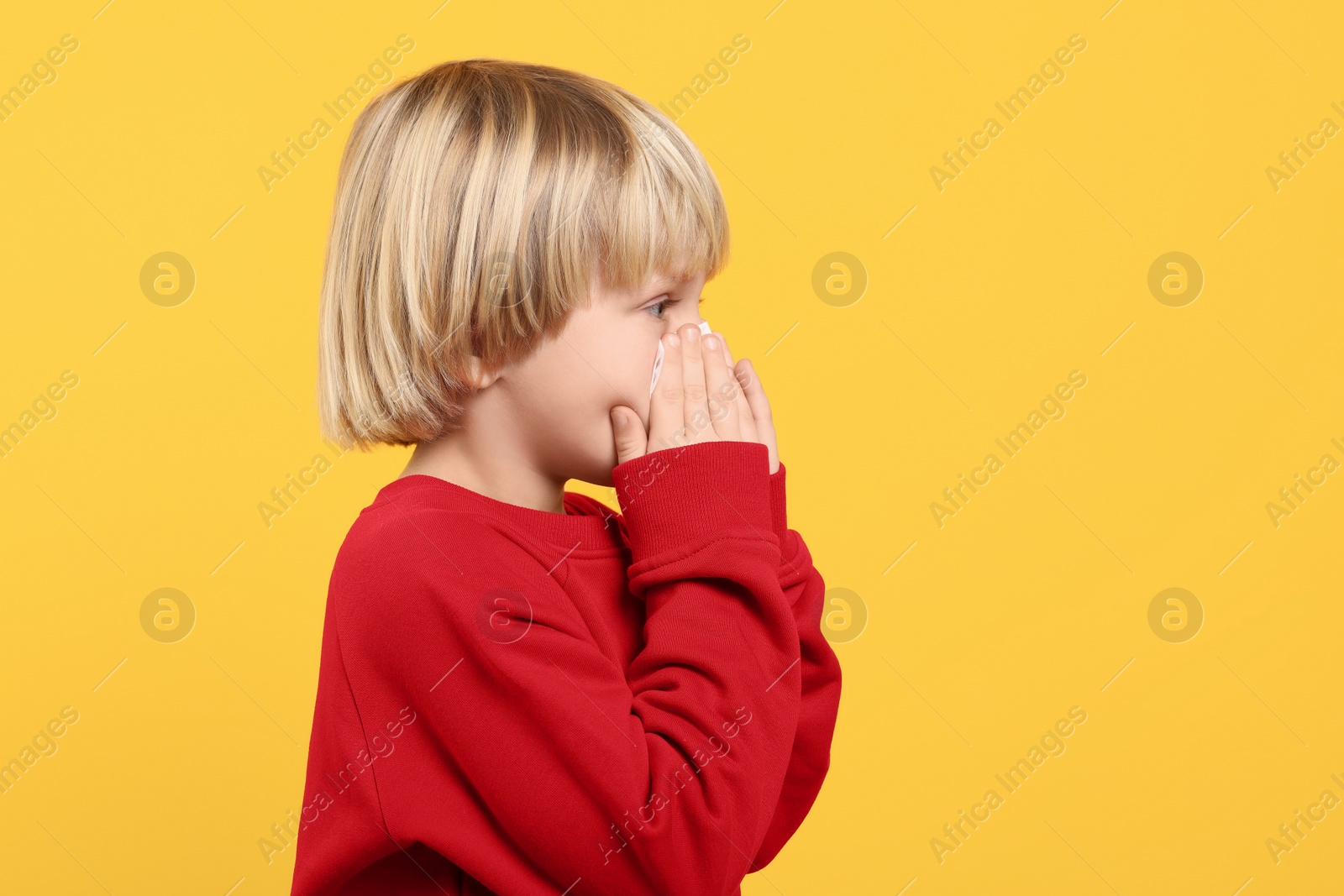 Photo of Boy blowing nose in tissue on orange background, space for text. Cold symptoms