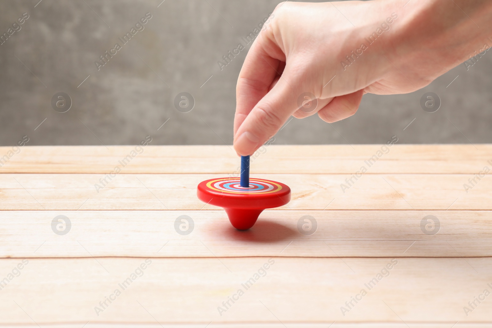 Photo of Woman playing with bright spinning top at light wooden table, closeup