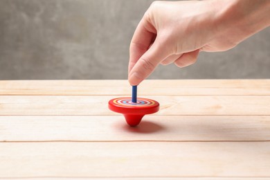 Woman playing with bright spinning top at light wooden table, closeup