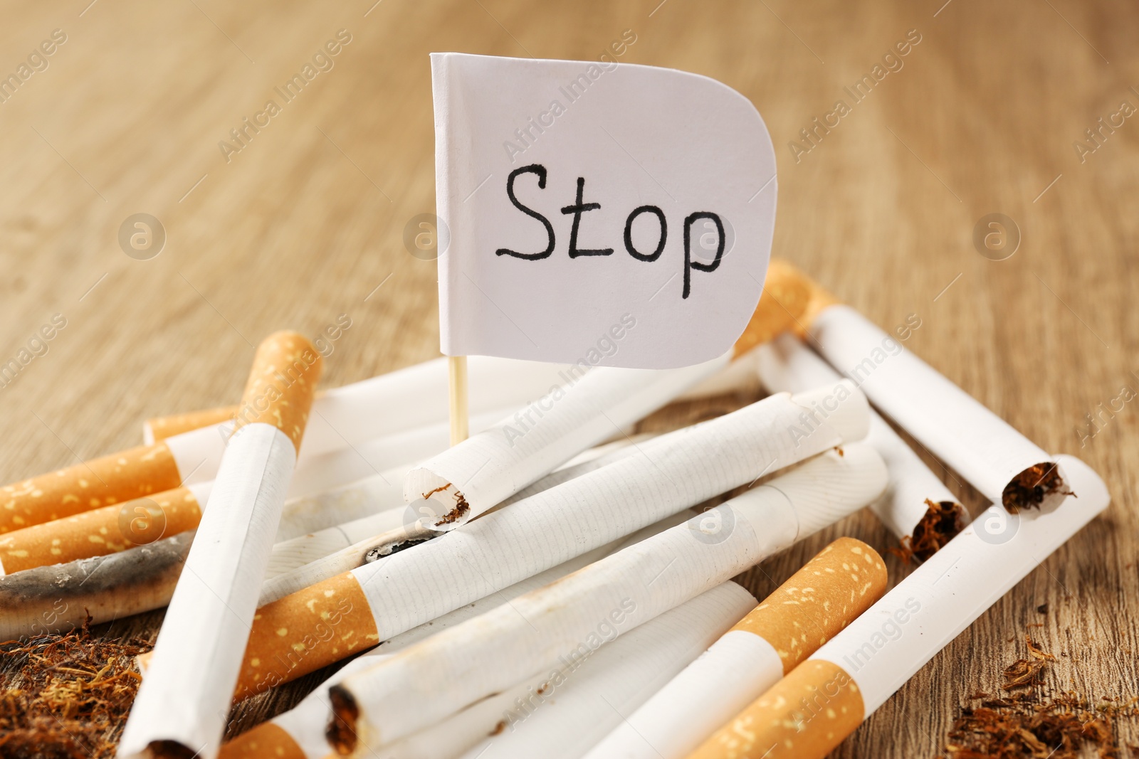 Photo of Pile of cigarettes and flag with word Stop on wooden table, closeup. No smoking concept